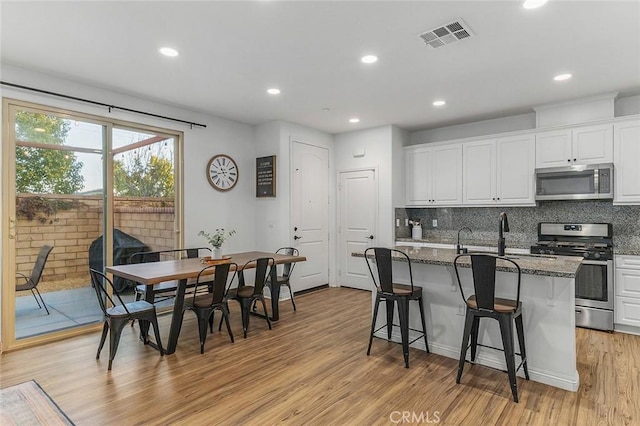 kitchen featuring appliances with stainless steel finishes, dark stone countertops, white cabinetry, and a kitchen island with sink