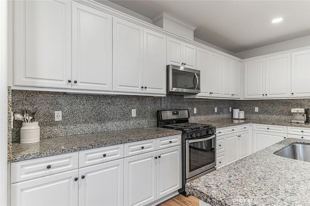 kitchen featuring white cabinets, decorative backsplash, appliances with stainless steel finishes, and dark stone countertops