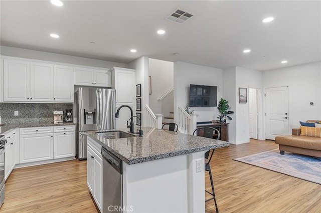 kitchen featuring a breakfast bar area, stainless steel appliances, white cabinets, and a center island with sink