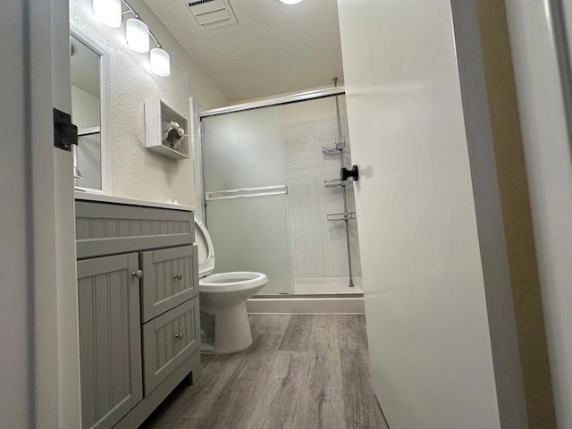 bathroom with a textured ceiling, wood-type flooring, vanity, toilet, and a shower with shower door