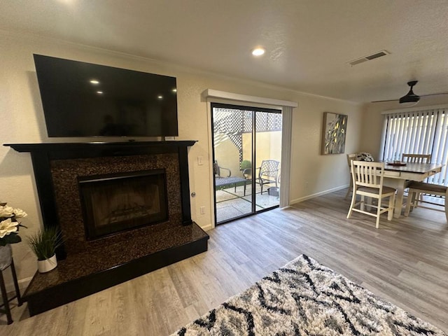 living room featuring a premium fireplace, ceiling fan, a wealth of natural light, and light hardwood / wood-style flooring