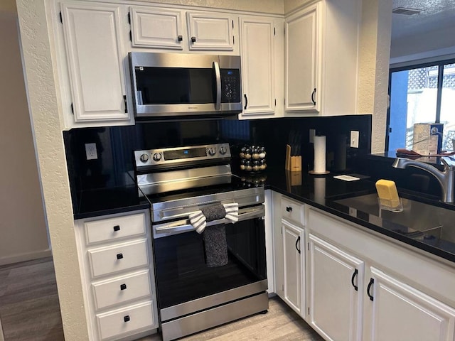 kitchen with appliances with stainless steel finishes, light hardwood / wood-style flooring, and white cabinets