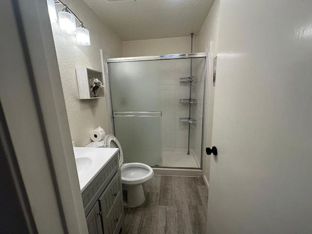 bathroom featuring hardwood / wood-style flooring, a shower with shower door, vanity, and toilet