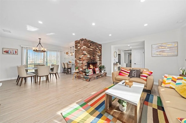 living room with a brick fireplace, light hardwood / wood-style floors, and a notable chandelier