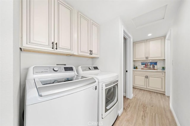 clothes washing area featuring cabinets, washing machine and clothes dryer, and light hardwood / wood-style floors