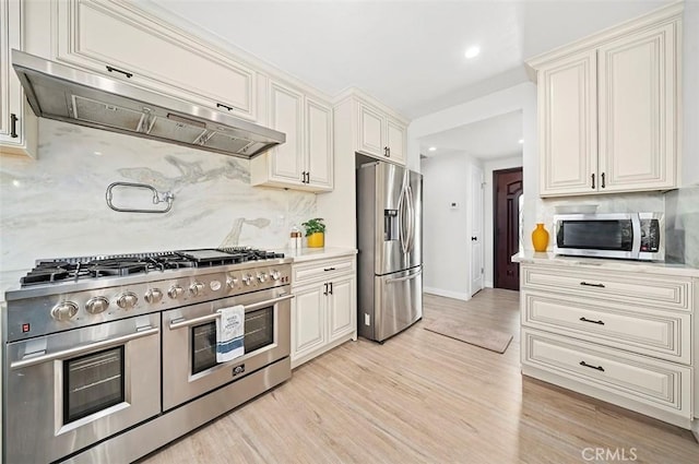 kitchen with white cabinetry, appliances with stainless steel finishes, tasteful backsplash, light wood-type flooring, and range hood