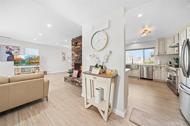 living room with a brick fireplace, sink, and light hardwood / wood-style floors