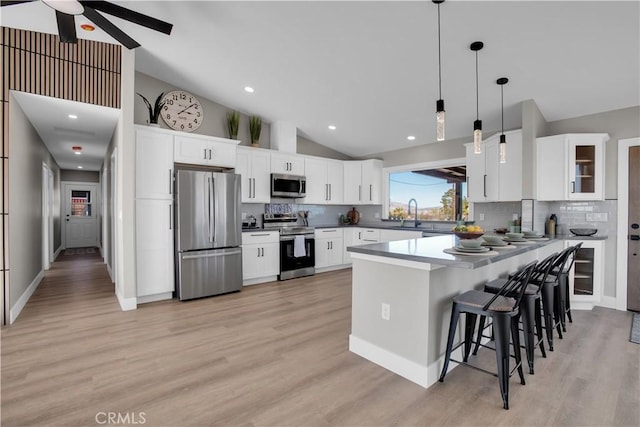 kitchen featuring pendant lighting, appliances with stainless steel finishes, white cabinetry, decorative backsplash, and light wood-type flooring