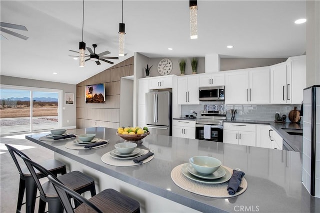 kitchen with vaulted ceiling, stainless steel appliances, pendant lighting, and white cabinetry