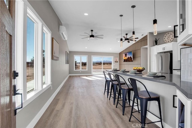 kitchen with a wall mounted AC, a kitchen bar, hanging light fixtures, stainless steel refrigerator, and white cabinets