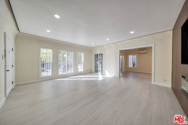 unfurnished living room with a wall mounted AC and light hardwood / wood-style floors