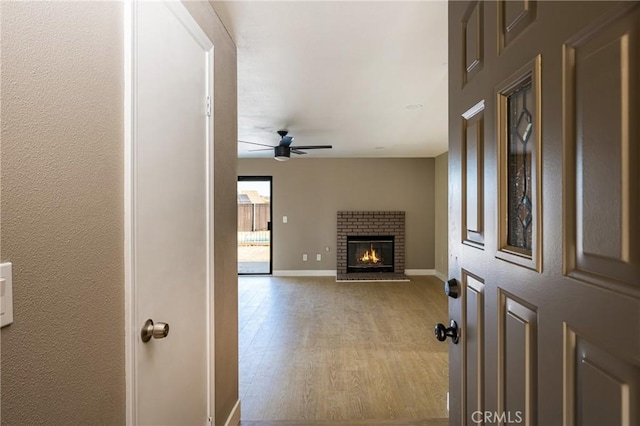 living room with ceiling fan, a brick fireplace, and light hardwood / wood-style flooring