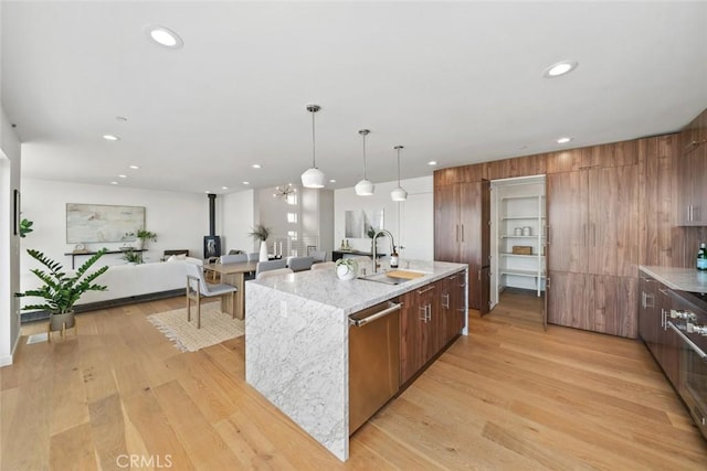 kitchen with pendant lighting, stainless steel dishwasher, sink, a kitchen island with sink, and a wood stove