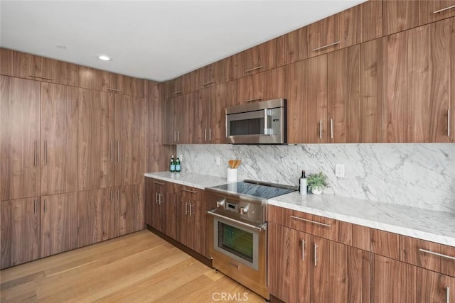 kitchen with light hardwood / wood-style floors, light stone counters, decorative backsplash, and appliances with stainless steel finishes