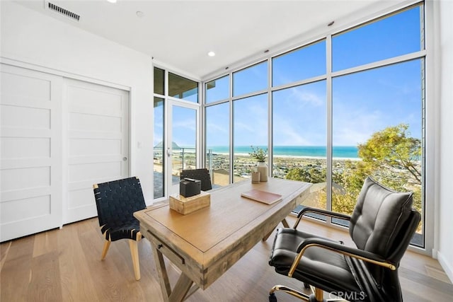 office area with light wood-type flooring, a water view, and expansive windows