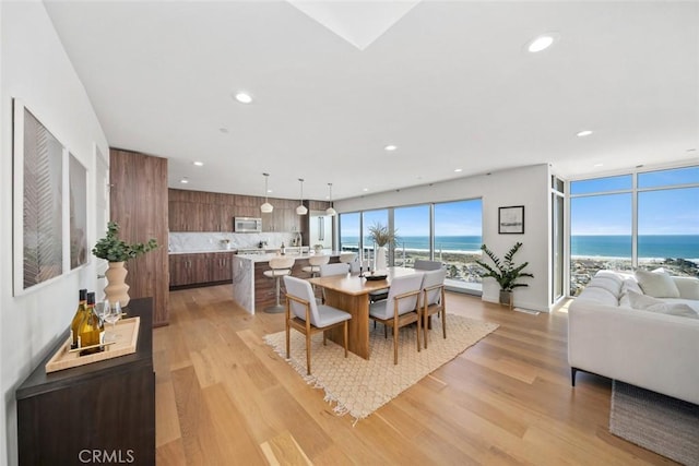 dining area with a water view, light wood-type flooring, and a beach view