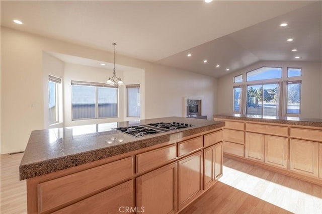 kitchen featuring light brown cabinets, light wood-style floors, vaulted ceiling, tile counters, and stainless steel gas stovetop