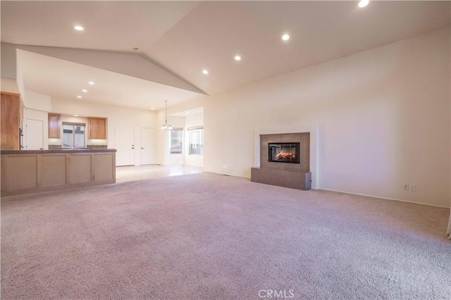 unfurnished living room with light carpet, recessed lighting, high vaulted ceiling, and a glass covered fireplace