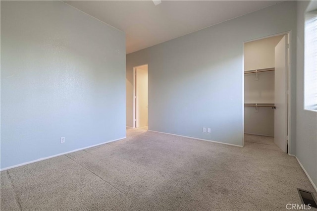 unfurnished bedroom with carpet floors, a closet, a walk in closet, and visible vents