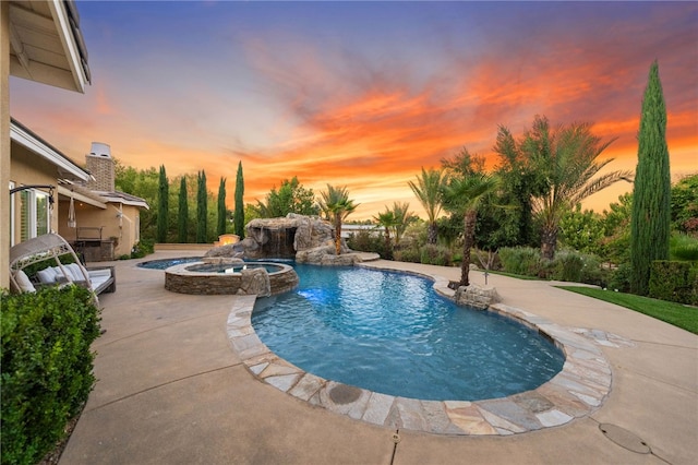 pool at dusk with pool water feature, a patio, and an in ground hot tub