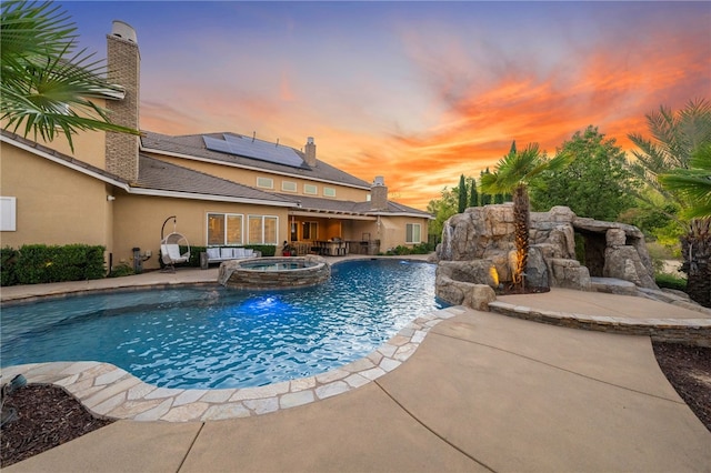 pool at dusk featuring a patio area and an in ground hot tub