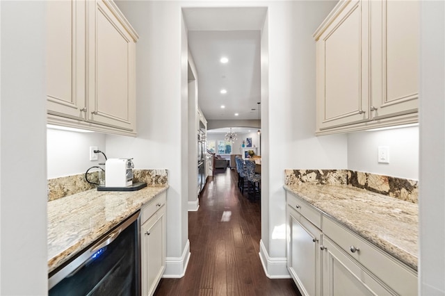 bar with light stone counters, dark wood-type flooring, stainless steel dishwasher, and cream cabinetry