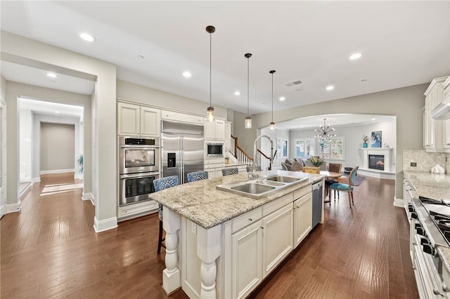 kitchen with pendant lighting, high end appliances, decorative backsplash, sink, and a center island with sink