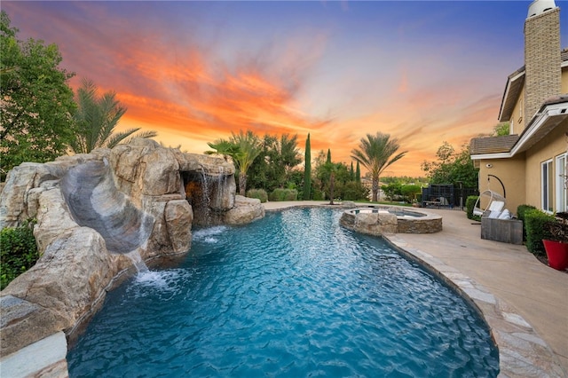 pool at dusk featuring pool water feature, a patio area, and an in ground hot tub