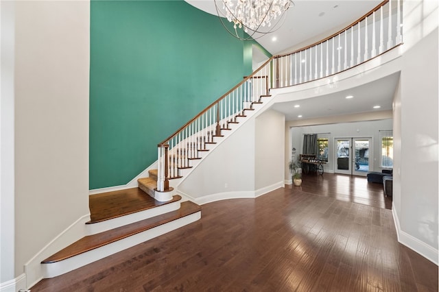 staircase with hardwood / wood-style flooring, a high ceiling, french doors, and an inviting chandelier