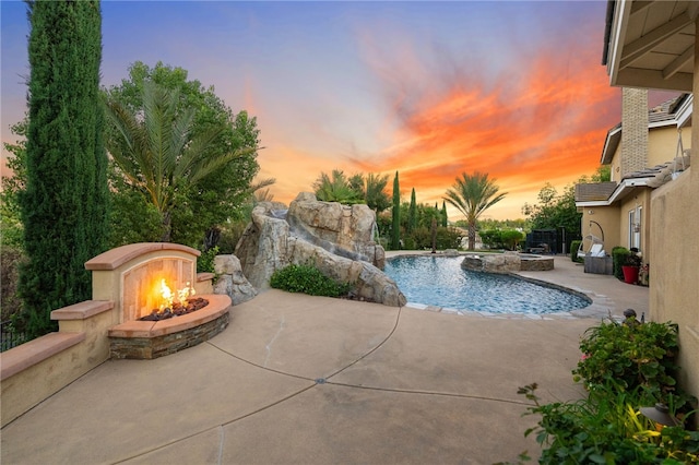 pool at dusk with a patio area, a fire pit, and pool water feature