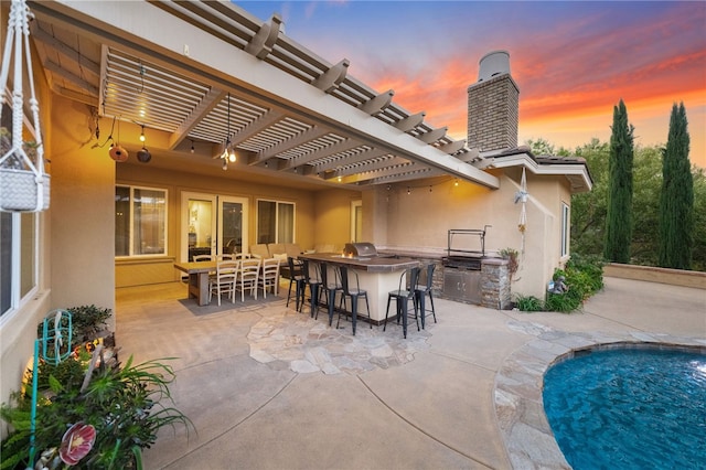 patio terrace at dusk featuring exterior kitchen, an outdoor bar, and a grill