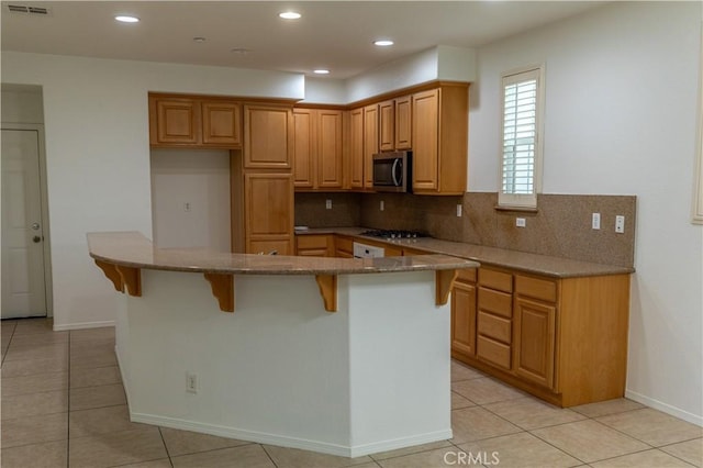 kitchen with decorative backsplash, appliances with stainless steel finishes, light tile patterned flooring, and a kitchen island