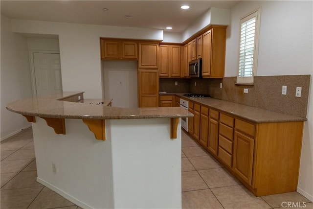 kitchen with backsplash, a kitchen island, a kitchen bar, stainless steel appliances, and light tile patterned floors