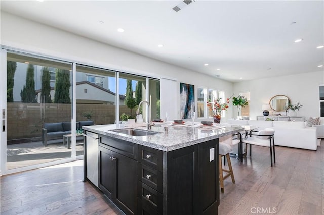 kitchen featuring a kitchen island with sink, sink, light stone counters, and hardwood / wood-style flooring