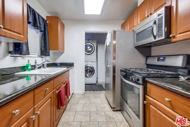 kitchen featuring stainless steel appliances, light tile patterned flooring, dark stone countertops, stacked washing maching and dryer, and sink