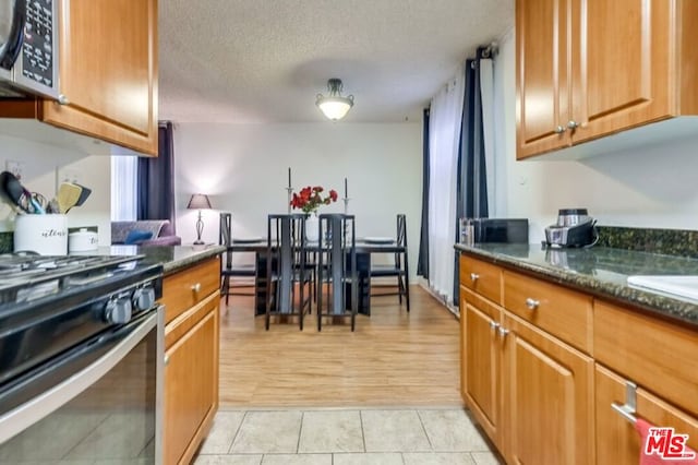 kitchen with black gas range oven, dark stone counters, light tile patterned flooring, and a textured ceiling