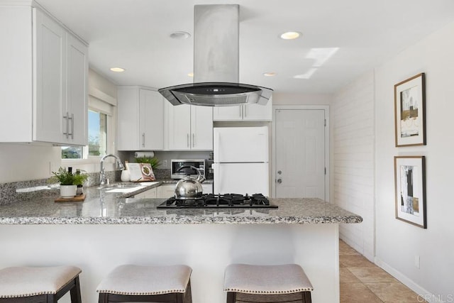 kitchen with white fridge, a kitchen bar, kitchen peninsula, island exhaust hood, and white cabinetry