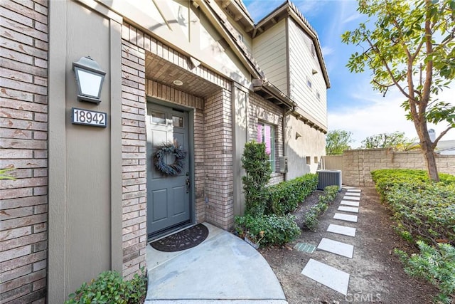 view of exterior entry featuring brick siding, central AC, and fence