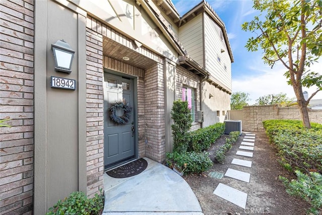 view of exterior entry featuring brick siding, fence, and central AC