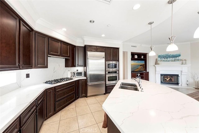 kitchen with ornamental molding, a sink, light tile patterned flooring, built in appliances, and a glass covered fireplace