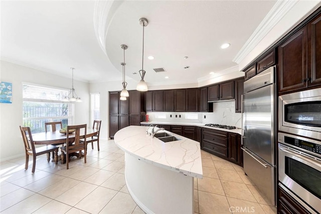 kitchen with visible vents, ornamental molding, a center island with sink, a sink, and built in appliances