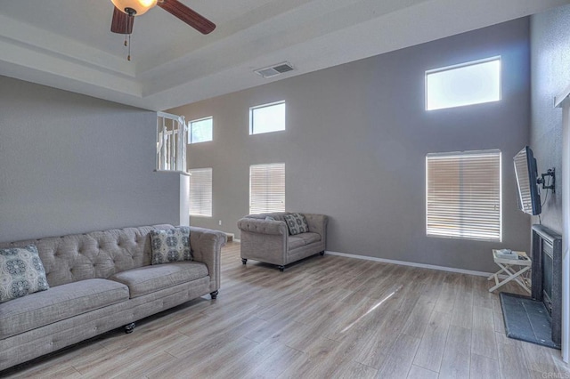 living room with light wood-type flooring, ceiling fan, a tiled fireplace, and a high ceiling