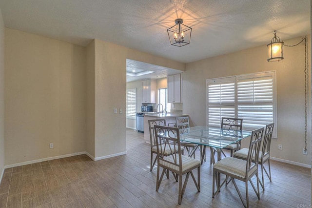 dining space with sink, an inviting chandelier, a textured ceiling, and light hardwood / wood-style floors