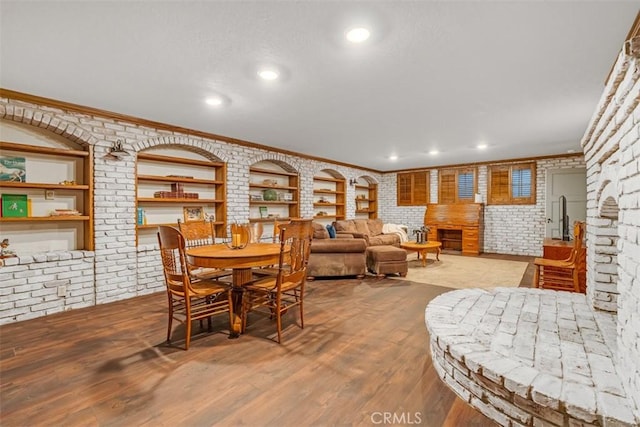 dining space with brick wall, crown molding, a fireplace, and wood-type flooring