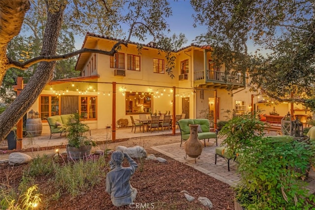 back house at dusk featuring a balcony and a patio