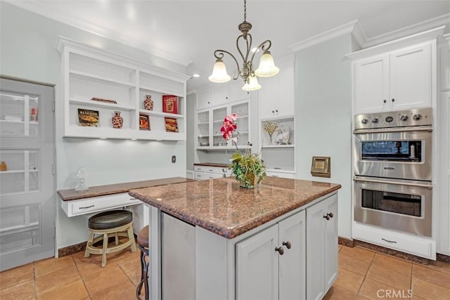 kitchen with stainless steel double oven, stone countertops, white cabinetry, and a center island