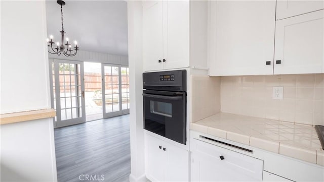 kitchen featuring black oven, white cabinets, tile counters, and tasteful backsplash