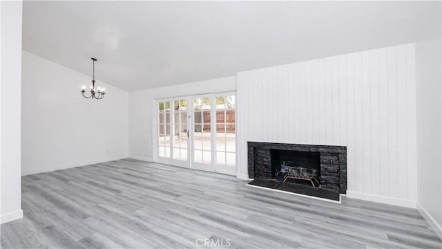 unfurnished living room with vaulted ceiling, a chandelier, light hardwood / wood-style floors, and a stone fireplace