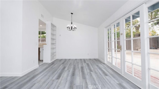 unfurnished dining area featuring lofted ceiling, a healthy amount of sunlight, an inviting chandelier, and light hardwood / wood-style flooring