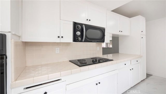 kitchen featuring tile counters, decorative backsplash, white cabinets, and black appliances